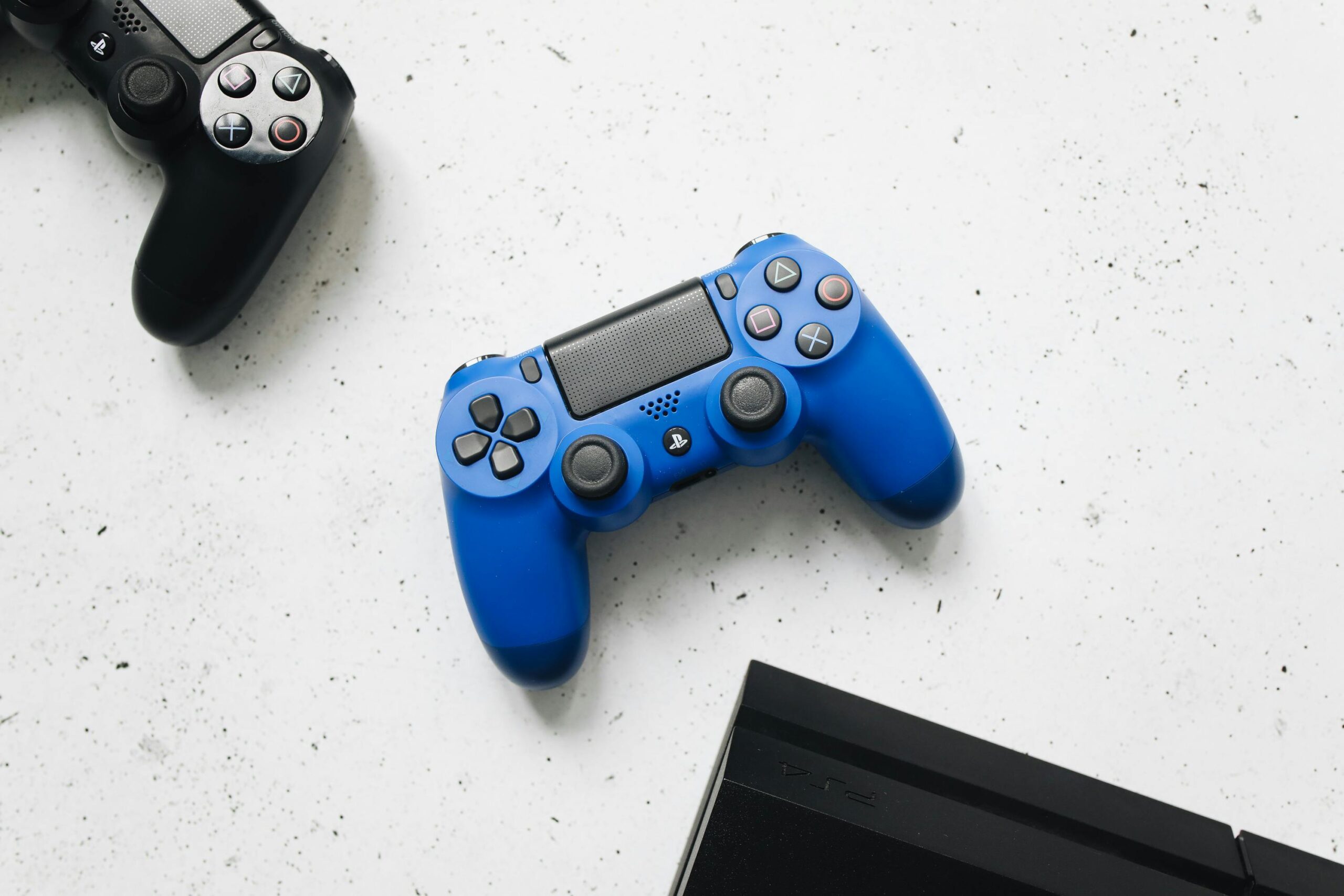 A close-up view of black and blue game controllers on a white speckled surface.